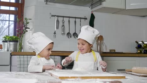 Dos-niñas-en-la-cocina-preparan-comida,-un-postre-para-la-familia.-Como-aprender-a-cocinar-empiezan-jugando-con-harina-y-sonriendo-unos-a-otros.