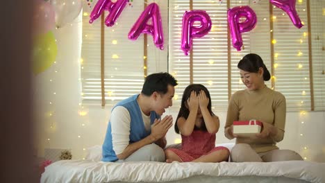 Happy-asian-family-celebrating-daughter's-birthday-opening-gifts-and-rejoice-on-bed.-Christmas,-happy-birthday-celebration.-New-Year-party.-Slow-motion.