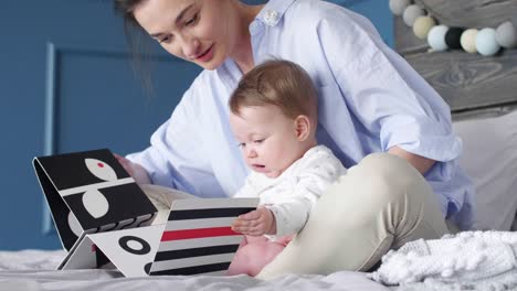 Joven-madre-y-bebé-viendo-un-libro-del-cuadro-en-el-dormitorio