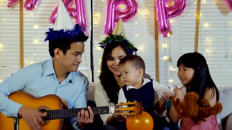 Father-playing-guitar-in-mini-party-at-home.-People-with-happy-family-and-party-concept.