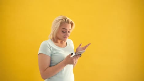 Überrascht-blond-plus-Größe-Modell-SMS-auf-Smartphone-auf-gelbem-Hintergrund-Slow-motion