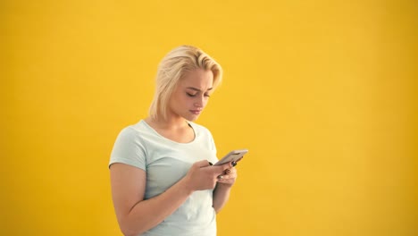 Rubia-sorprendida-más-tamaño-modelo-de-mensajes-de-texto-en-el-teléfono-inteligente-en-cámara-lenta-de-fondo-amarillo