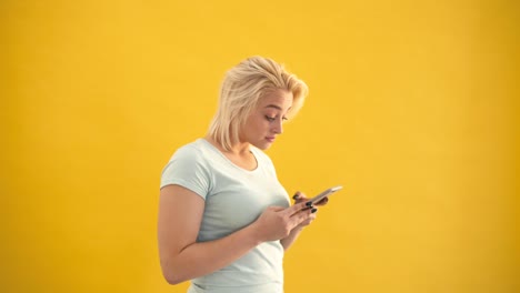 Unglücklich-Blond-plus-Größe-modellieren-überrascht-Überprüfung-Nachricht-am-Telefon-auf-gelbem-Hintergrund