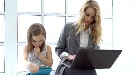 Junge-Geschäftsfrau-mit-Laptop-und-kleine-Mädchen-sitzen-am-Fenster.