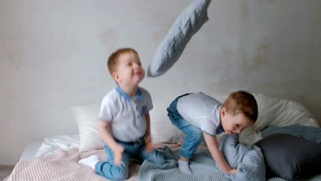 Twin-boys-toddlers-are-lying-on-the-bed,-throwing-pillows,-jumping-and-laughing.
