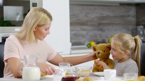 Niña-y-madre-de-alimentación-del-oso-juguete-en-el-desayuno