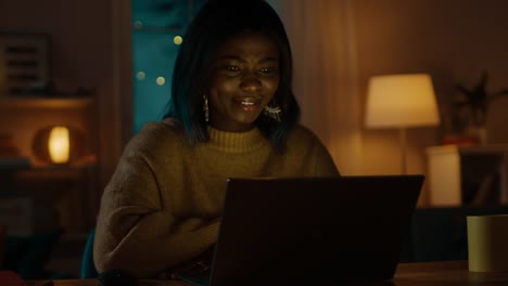 Porträt-von-schönen-lächelnden-schwarze-Mädchen-sitzt-an-ihrem-Schreibtisch-mit-Laptop,-einen-Videoanruf-tätigen-lässt-grüßen.-In-den-Abend-Mädchen-Gespräche-mit-Verwandten-und-Freunden-mit-Computer-Webcam.