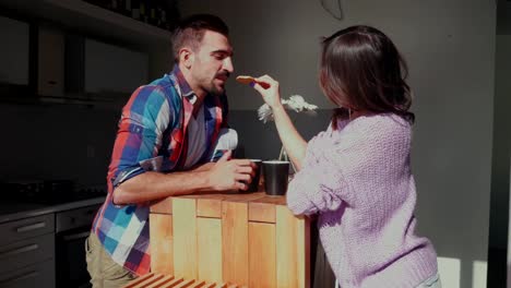 Woman-feeding-smiling-boyfriend-with-a-cookie-in-the-kitchen