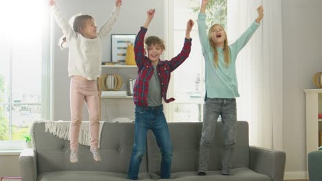 Zwei-niedliche-kleine-Mädchen-und-junge,-bezaubernde-haben-Spaß,-springen-hoch-auf-einer-Couch-zu-Hause.-Happy-Kids-tanzen-auf-einem-Sofa-im-sonnigen-Wohnzimmer.-In-Zeitlupe.