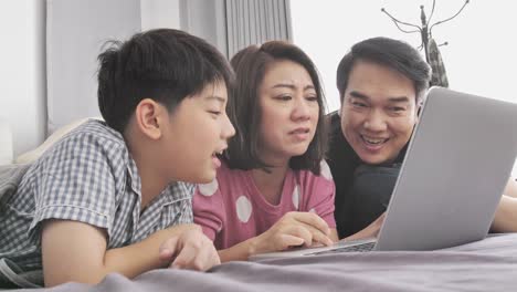 Glückliche-Familie-Vater-Mutter-und-Sohn-auf-Laptop-Computer-beobachten-und-Spaß,-Slow-Motion-4K-asiatischen-Familie-Rest-auf-Bett-mit-Laptop-computer