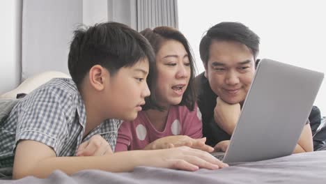 Glückliche-Familie-Vater-Mutter-und-Sohn-auf-Laptop-Computer-beobachten-und-Spaß,-Slow-Motion-4K-asiatischen-Familie-Rest-auf-Bett-mit-Laptop-computer