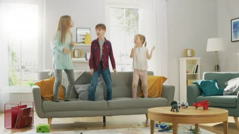 Zwei-niedliche-kleine-Mädchen-und-junge,-bezaubernde-haben-Spaß,-springen-hoch-auf-einer-Couch-zu-Hause.-Happy-Kids-tanzen-auf-einem-Sofa-im-sonnigen-Wohnzimmer.