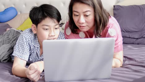 Happy-family-Mother-and-Son-watching-on-laptop-computer-with-smile-face-,-Slow-motion-4K--asian-family-rest-on-bed-with-laptop-computer