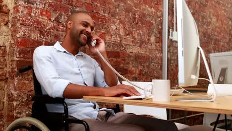 Casual-businessman-in-wheelchair-working-at-his-desk