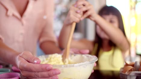 Kleines-Mädchen-Rühren-Kuchen-Zutaten-mit-Ihr-kleines-Mädchen-fröhlich-Rühren-Kuchen-Zutaten-in-Schüssel-mit-einem-Holzlöffel-mit-ihrer-Mutter-in-Ihre-kitchenmom