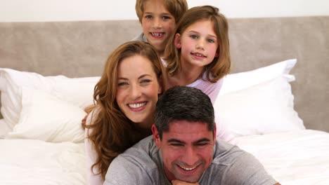 Cute-parents-and-children-lying-on-bed-smiling-at-camera