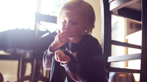 Pequeña-niña-sentada-en-el-piso-de-la-cocina-y-comiendo-azúcar-en-polvo,-destello-de-lente