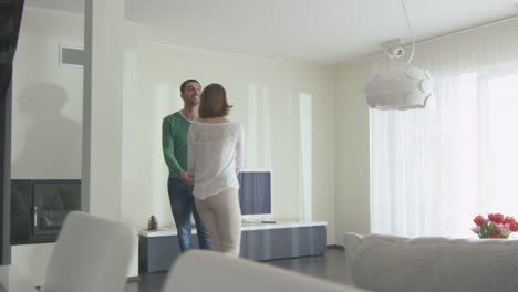 Happy-couple-are-walking-into-a-new-home-and-looking-around-the-apartment.