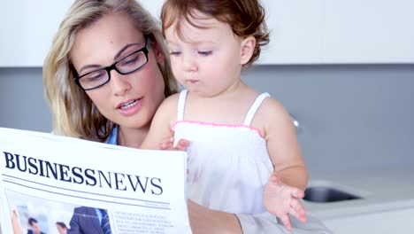 Madre-rubia-leyendo-el-diario-con-su-bebé-en-la-piedra-de-afilar