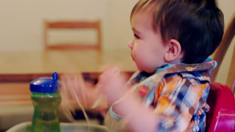 Adorable-baby-boy-sitting-in-a-high-chair-booster-seat-and-eating-spaghetti-with-his-hands