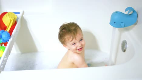 Adorable-little-boy-sits-in-the-bathtub-as-the-water-fills-up,-and-he-dries-drinking-the-water