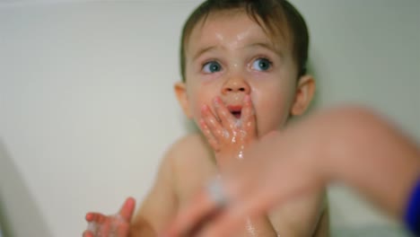 Adorable-niño-se-sienta-en-la-bañera-y-lame-sus-manos-jabonosas