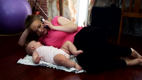 Young-mother-lie-on-floor-with-little-baby,-speak-on-phone.-Apartment.-Family