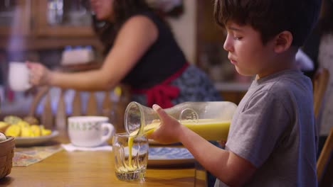 A-boy-pouring-orange-juice-from-a-pitcher-into-a-glass,-at-the-table