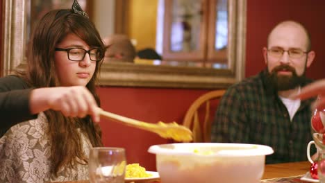 Young-girl-scoops-food-onto-plate-and-passes-dish-to-dad-at-dinner-table