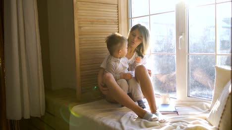 Mutter-mit-Baby-sitzt-am-Fenster-und-spielt