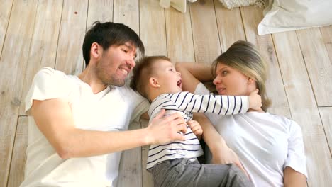 Top-view-of-handsome-father-and-mother-play-and-hug-their-little-son-while-lying-on-the-floor