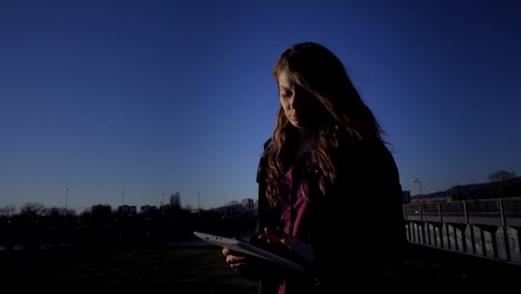 Mujer-utilizando-tablet-fuera-al-atardecer