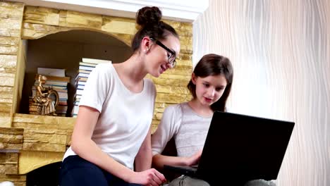 girl-wearing-glasses-watching-her-small-sister-doing-her-homework-at-laptop,-teens-sitting-together