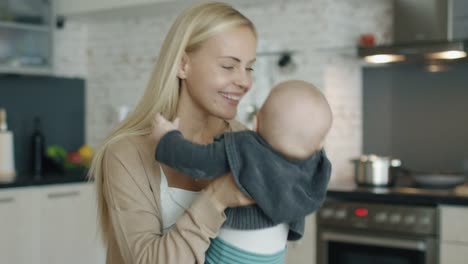 Joven-madre-tiene-y-juega-con-su-bebé-mientras-de-pie-en-la-cocina