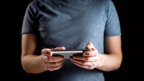 Concept,-digital-online-life-and-social-networks.-A-businessman-in-a-t-shirt-uses-his-smartphone-to-view-his-accounts.-Expressive-shot,-a-man-in-a-dark-room,-holding-a-stylish-phone