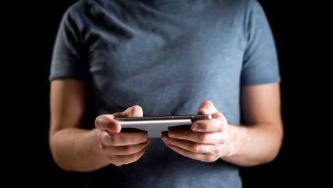 Concept,-digital-online-life-and-social-networks.-A-businessman-in-a-t-shirt-uses-his-smartphone-to-view-his-accounts.-Expressive-shot,-a-man-in-a-dark-room,-holding-a-stylish-phone