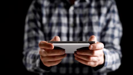 Concept,-digital-online-life-and-social-networks.-A-businessman-in-a-shirt-uses-his-smartphone-to-view-his-accounts.-Expressive-shot,-a-man-in-a-dark-room,-holding-a-stylish-phone