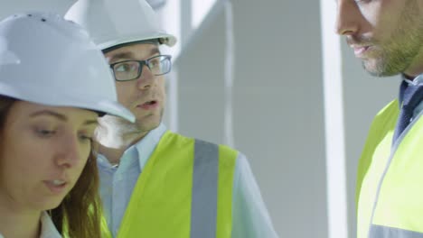 Team-von-Ingenieuren-in-Hard-Hats-Haben-Konversation,-Blick-auf-die-Blaupause,-in-Gebäude-Unter-Bau.