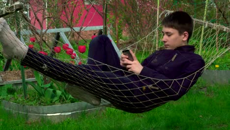 4K-Portrait-boy-Playing-Tablet-in-Hammock,-the-young-man-Face-Use-Smart-Phone-in-Nature