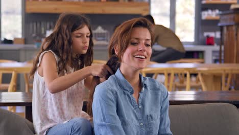 Tochter-Zöpfen-Mutters-Haare,-wie-sie-auf-Lounge-Sofa-sitzen