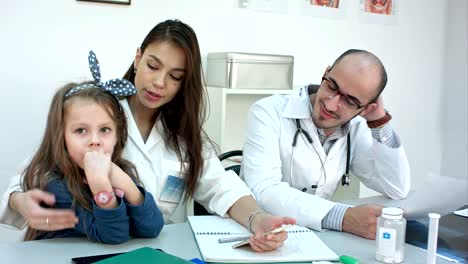 Llevar-tu-hija-al-trabajo-día.-Enfermera-de-la-madre-hablando-a-su-niña-mientras-estaba-sentado-en-la-oficina-con-un-compañero-de-trabajo-hombre