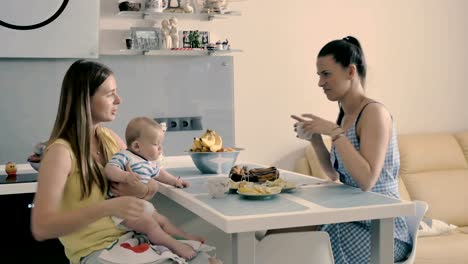 Joven-madre-con-bebé-bebe-un-té-con-su-amigo-en-la-cocina-en-casa