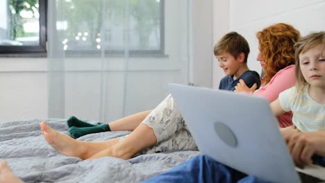 Familie-auf-Bett-mit-Kindern-mit-Tablet-und-Laptop-Computer-im-Schlafzimmer-zusammen