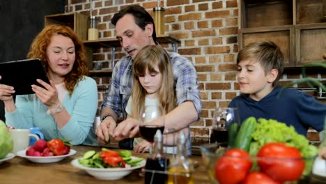 Vater-und-Tochter-Hacken-Gemüse-kochen-zusammen-In-der-Küche,-im-Gespräch-mit-Sohn-und-Mutter-mit-Tablet-Digitalrechner-glückliche-Familie-zu-Hause-zu-kommunizieren