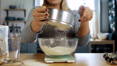 Vista-de-primer-plano-de-hermosa-mujer-joven-pesa-la-harina-usando-escalas-de-la-cocina,-recipiente-y-tamiz-para-esto