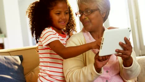 Smiling-grandmother-and-granddaughter-using-digital-tablet-on-sofa-in-living-room-4k