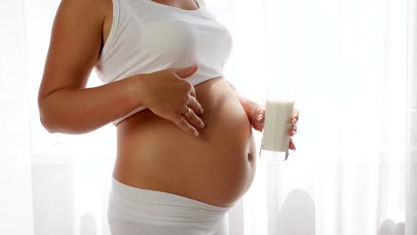 Mutter-mit-großen-Bauch-hält-Glas-Milch-und-Daumen-auftaucht,-in-Zeitlupe,-gesunde-Ernährung