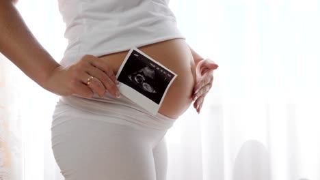 female-massages-her-big-tummy-in-slow-motion-and-holds-scan-of-future-baby-near-belly