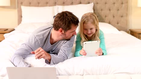 Happy-father-and-daughter-lying-on-bed-using-laptop-and-tablet-4K-4k