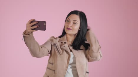 Lächelnde-glücklich-Brünette-Frau-in-rosa-Jacke-Selfie-auf-Smartphone-über-farbigen-Hintergrund-machen.-4k